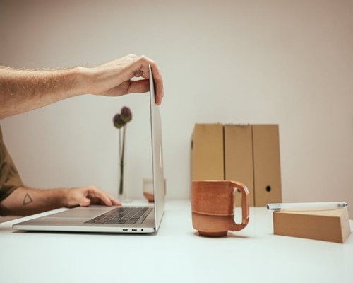 Person adjusting laptop screen angle at a well-lit wooden desk